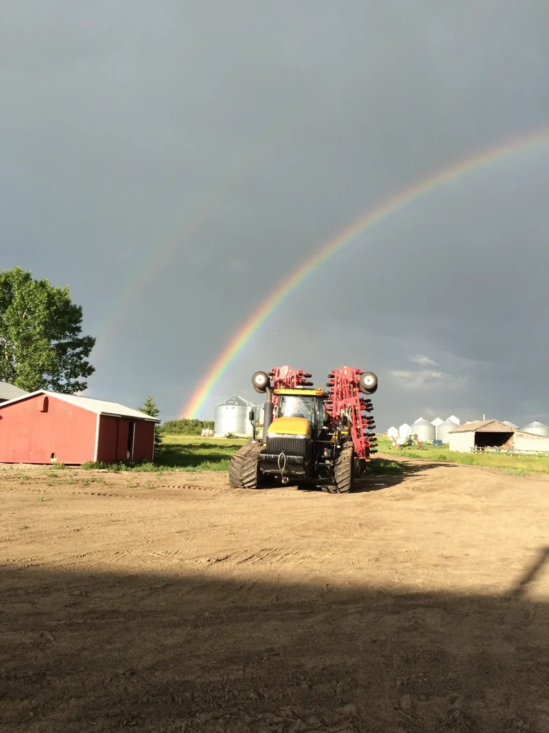 Rainbow above a tractor, red barn and grain bins in the farmyard